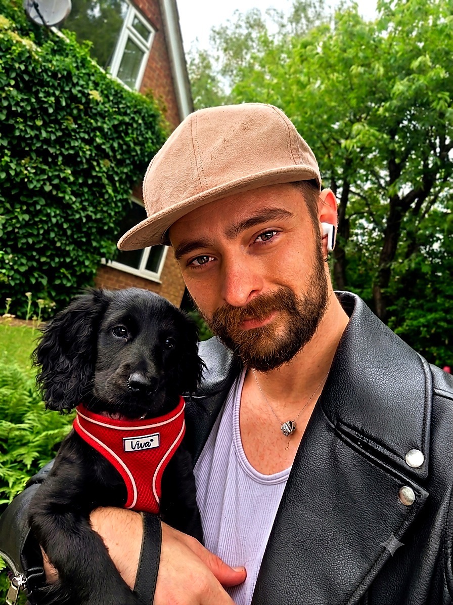 Jay holding Arwyn, a young black cockapoo in a red harness, outside in front of an ivy-covered house in Beverley